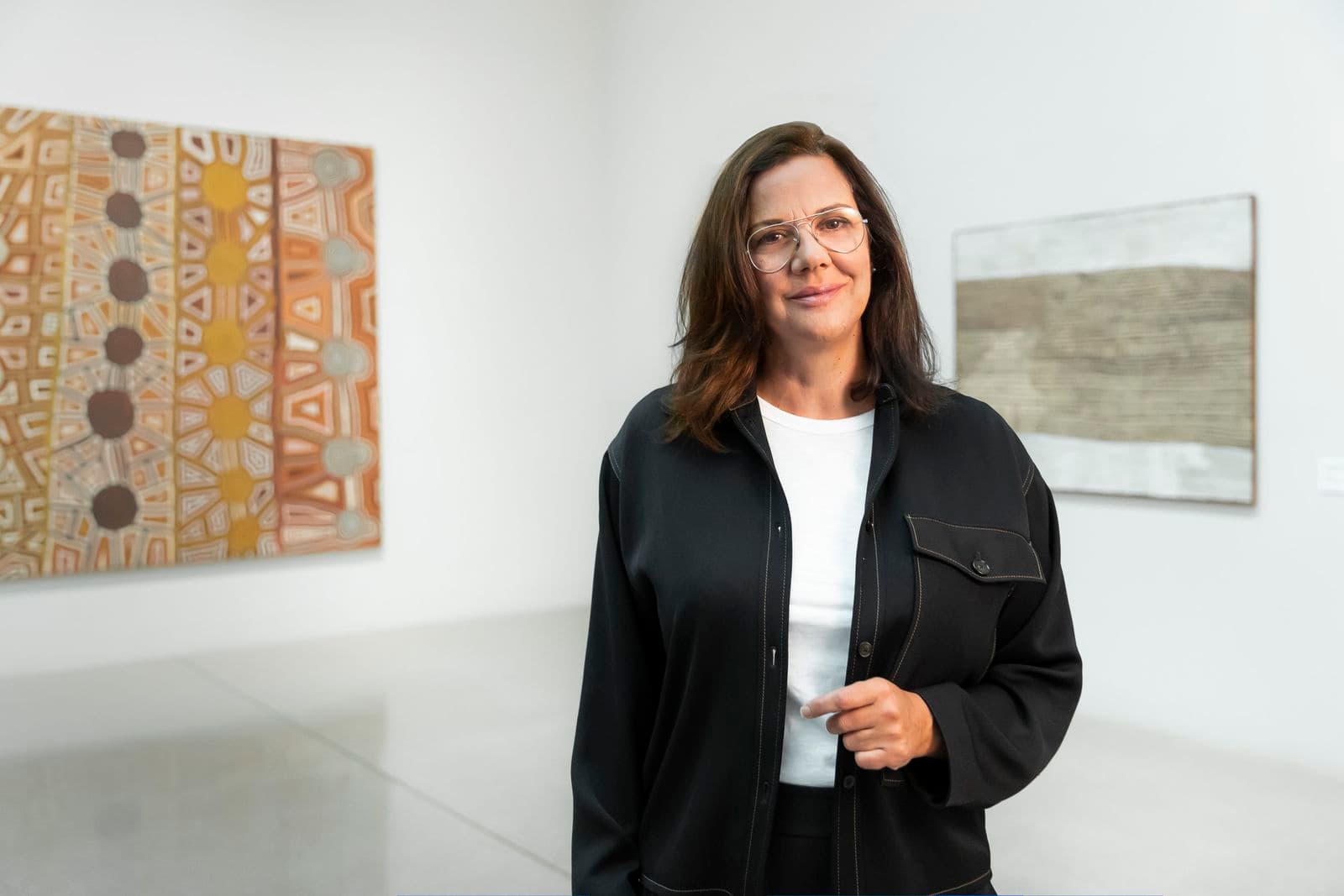 Hetti Perkins stands in front of two artworks.