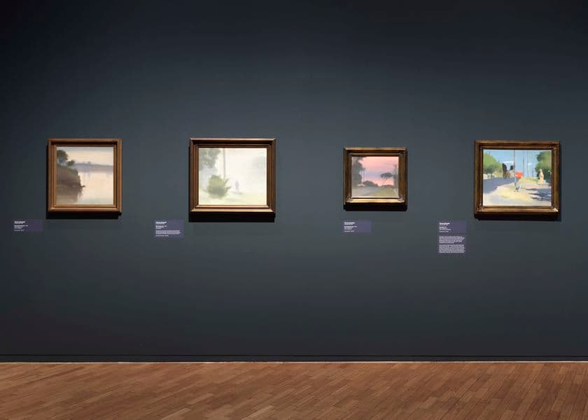 A dark grey wall with four works of art on it