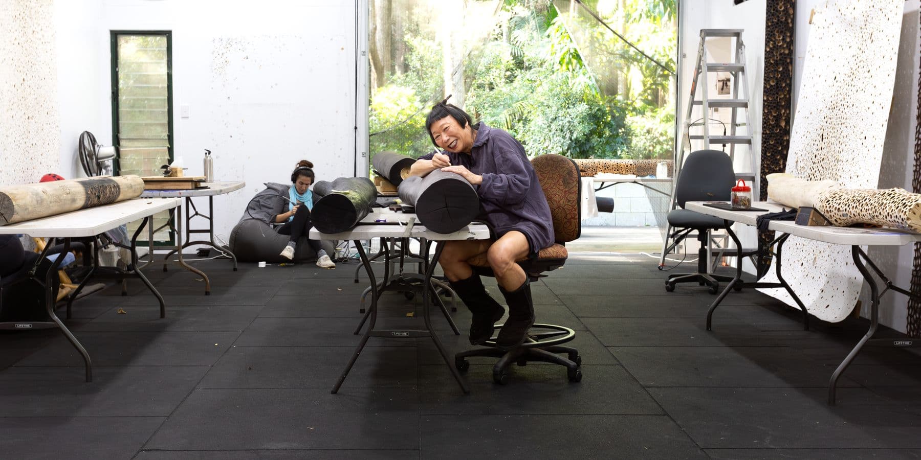 A woman sits drapped over a large round object in a busy studio.