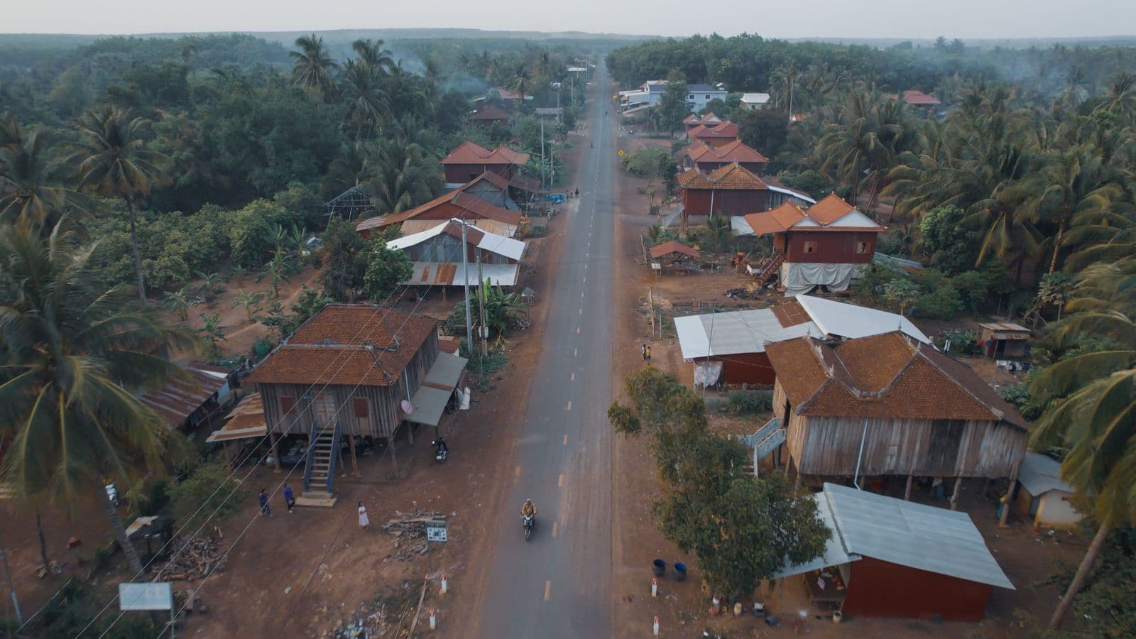 A photo of a man riding a motorbike through a village