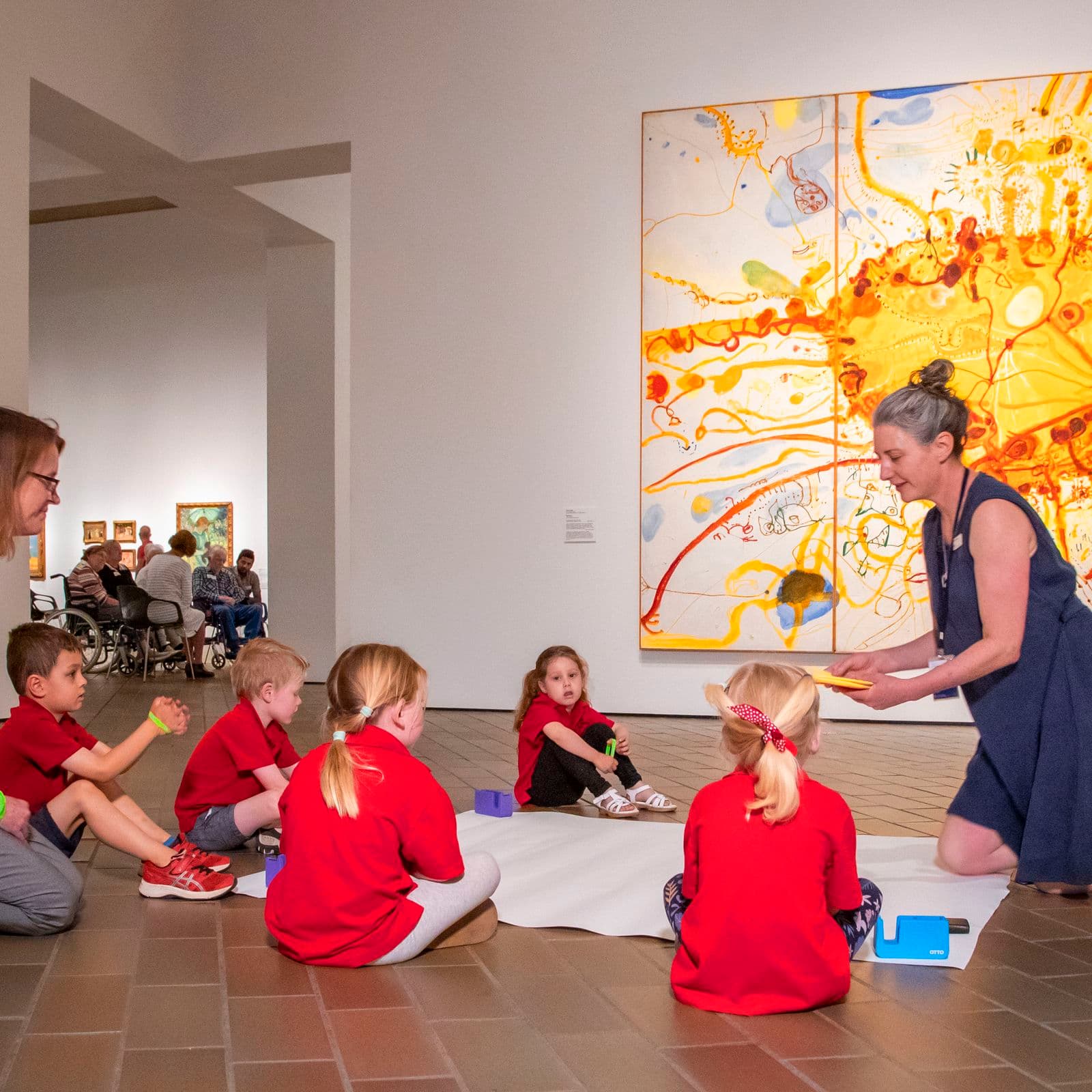 A group of primary school children and their teachers sit on the gallery floor and work together on an artwork