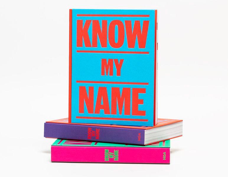 Photograph of three versions of the same book, all in different colours. One is standing upright on top of two laying flat.