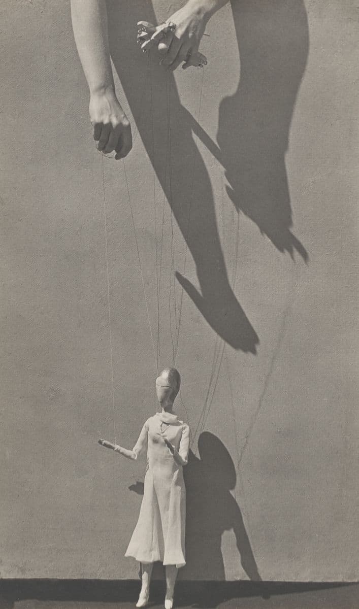 A picture of two hands holding the strings to a wooden human figure doll in black and white