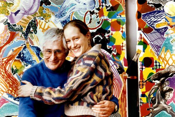 A couple embrace in front of a colourful artwork