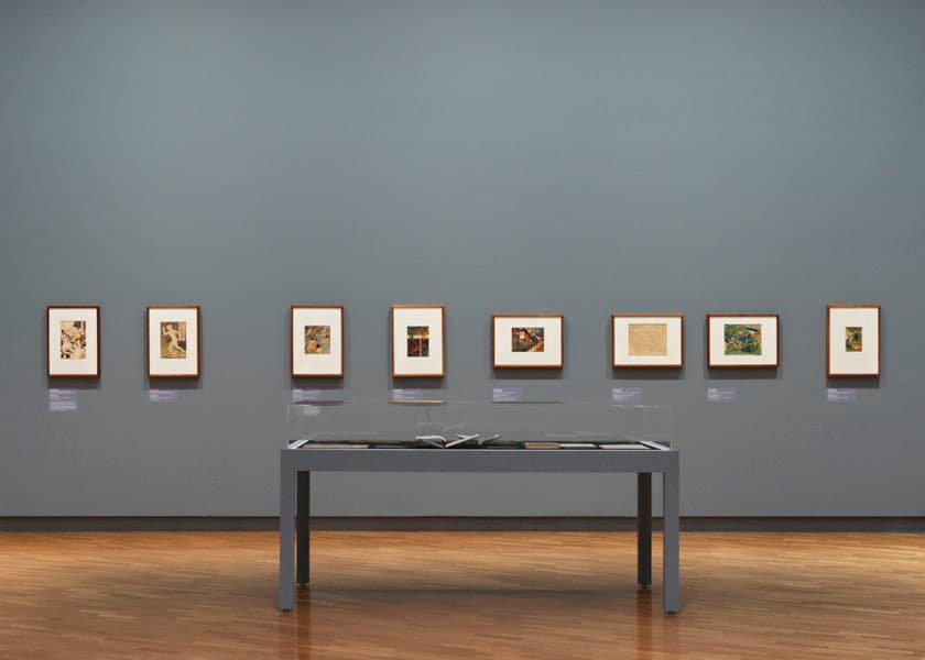 A light grey wall with eight small works of art hung on the wall