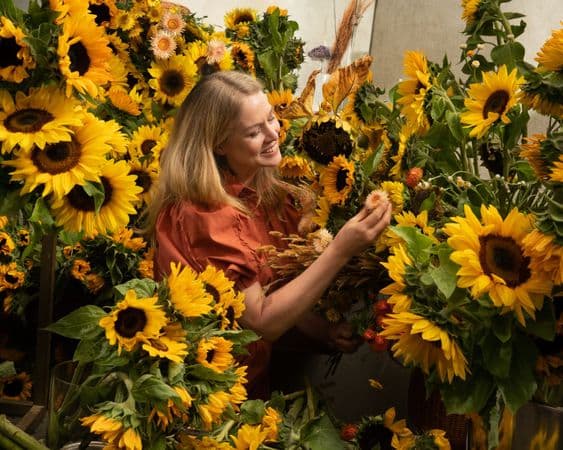A woman is surrounded completely by a collection of sunflowers and other yellow flowers