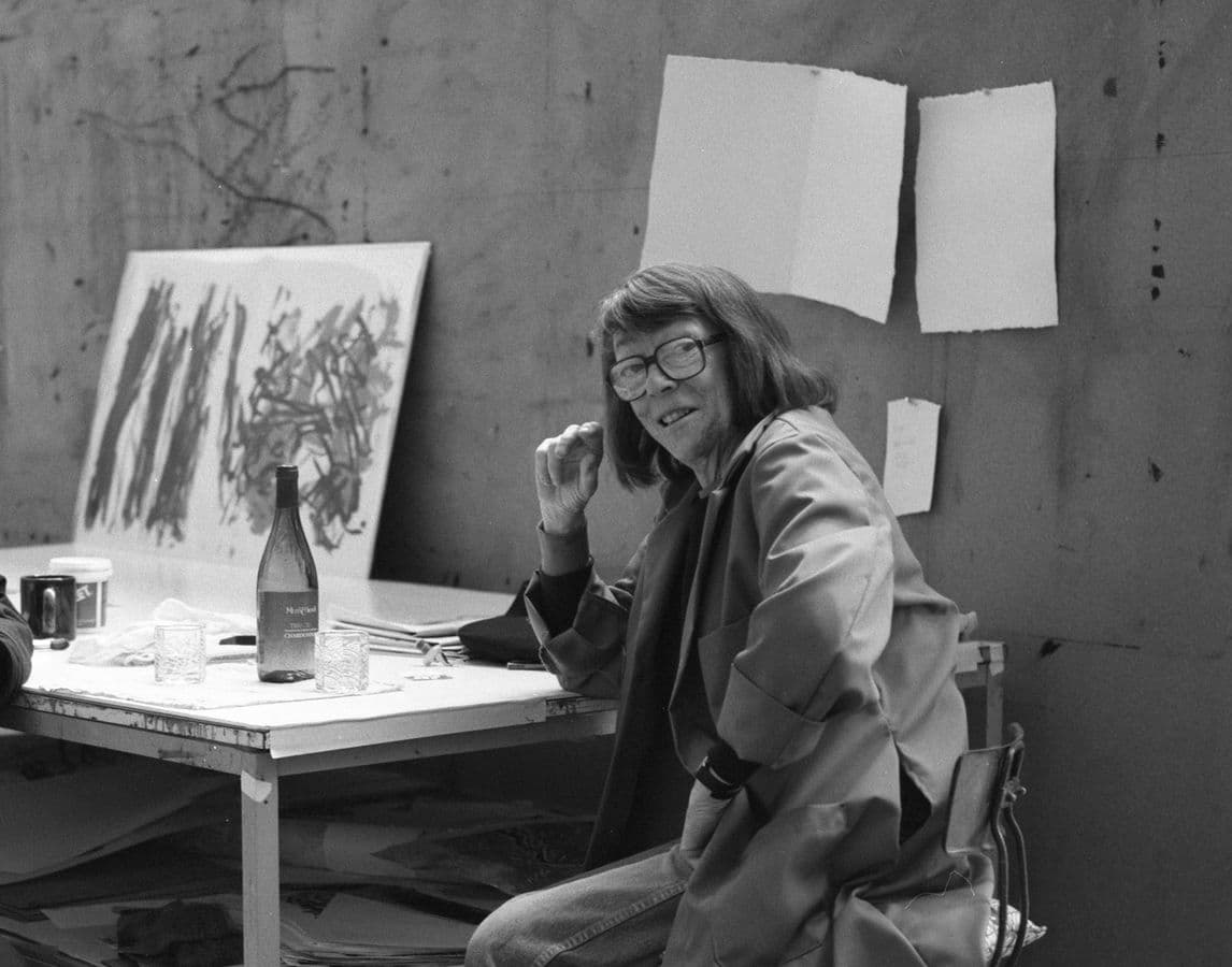 Black and white photo of artist Joan Mitchell sitting at table