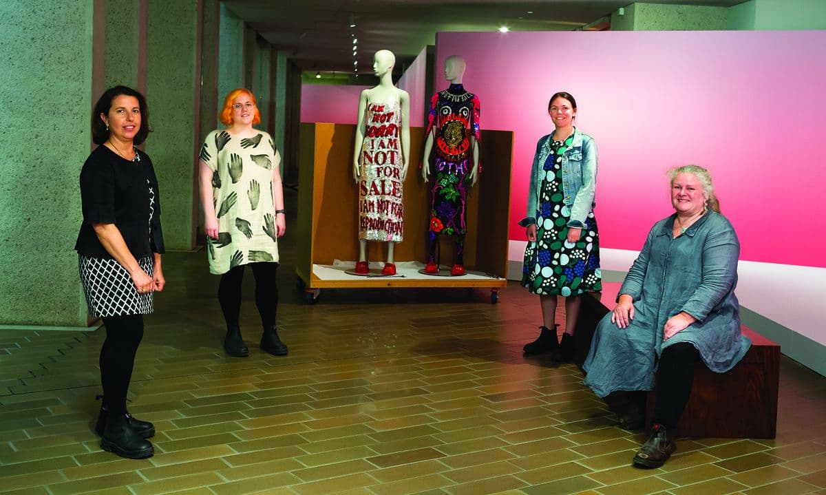 A team of four conservators stands in front of two dressed mannequins