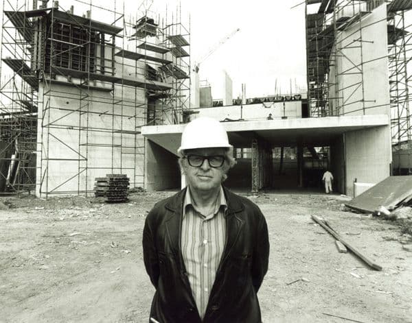 Black and white portrait of a mean wearing a hard hat in front of a building under construction