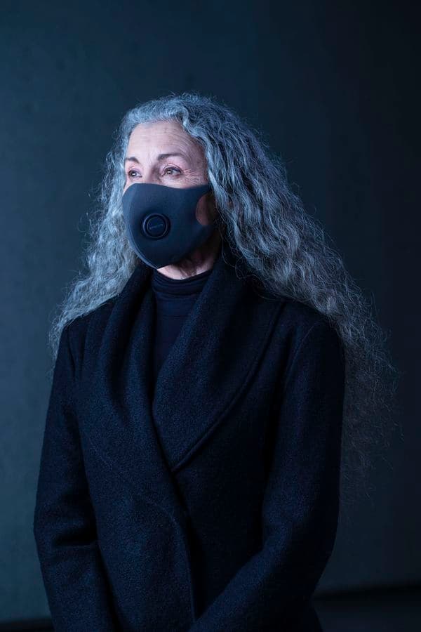 Photo of artist wearing black face mask with long greying hair