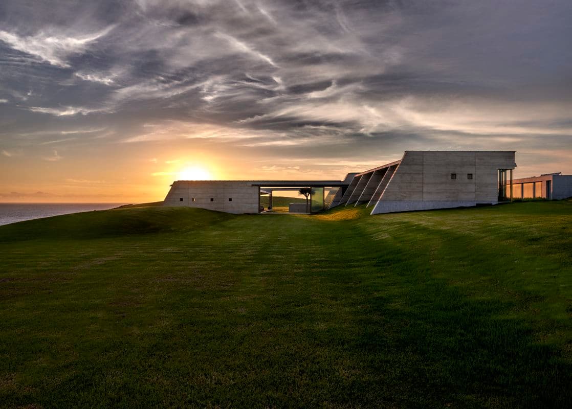 Photograph of grey building on grass at sunset
