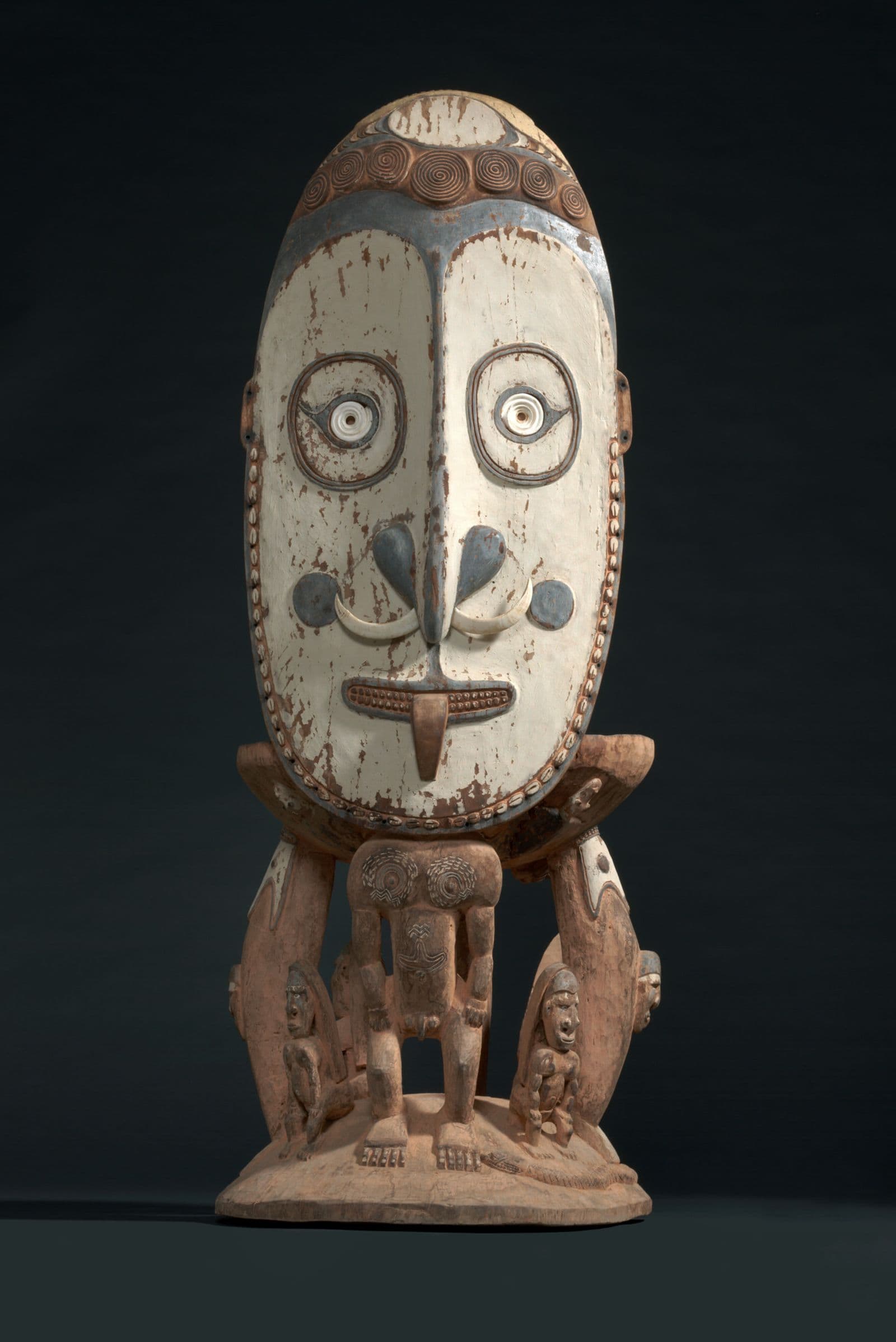 Stool backing with traditional figure with oversized head, facial decoration and paint, two smaller figures lie at base