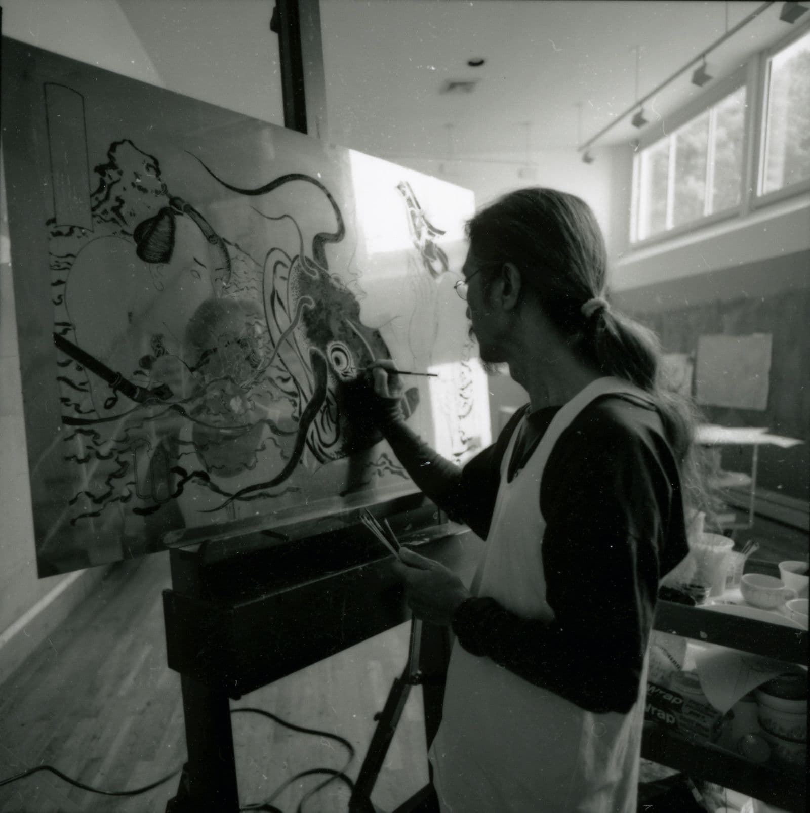 A blurry black and white photograph of Masami Teraoka painting.