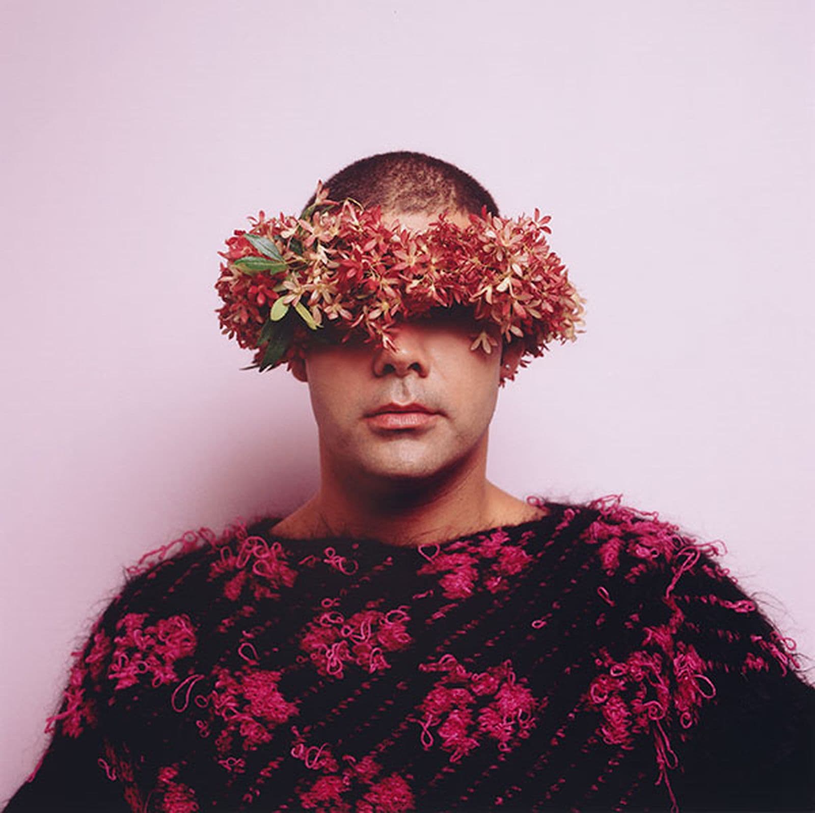 A man stands in front of a pink background wearing a crown of native Australian blossoms covering his eyes