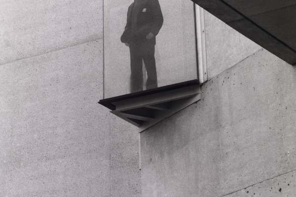 A man standing in the architectural glass window of the National Gallery looking out