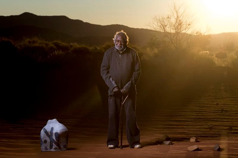 Photograph of an elderly man, the artist, standing in a desert next to a vase