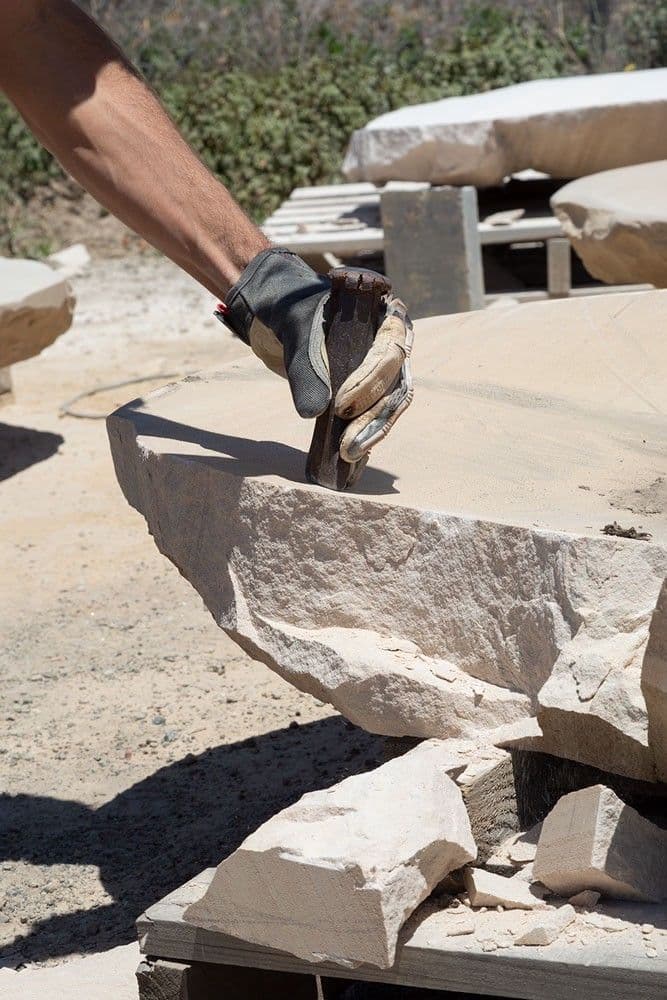 A hand holds a chisel to rock