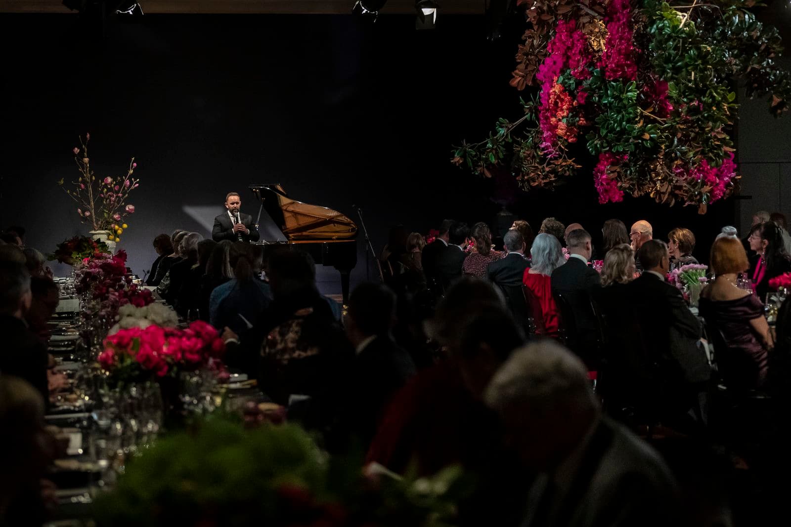 Photograph of gala dinner with guests seated amongst flowers and speaker in distance