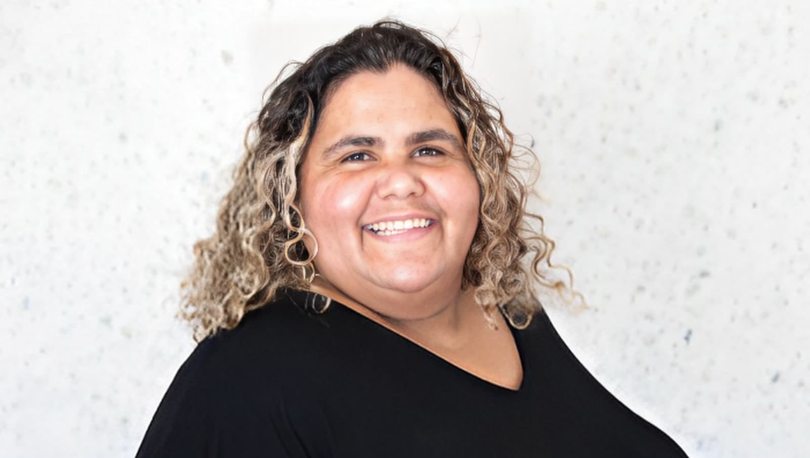 Photo of a smiling woman with curly hair in a black shirt