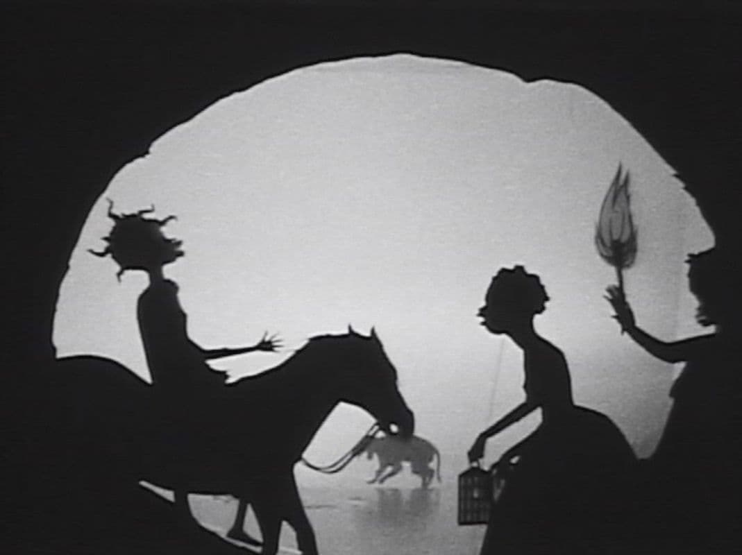 A black and white still of a silhouette film work showing a figure on a horse, a woman and a figure holding a flaming torch