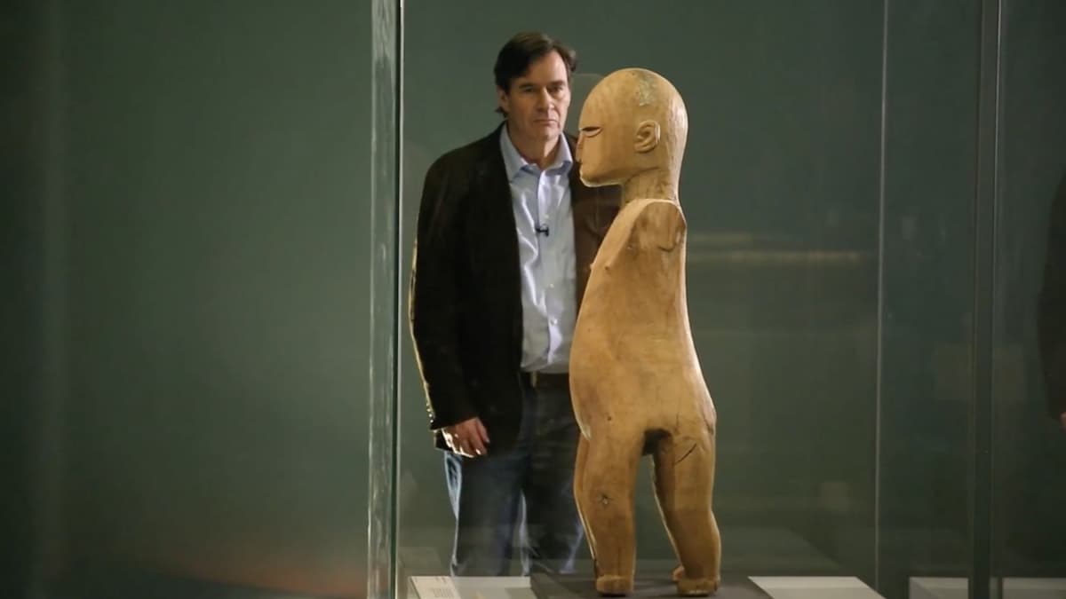 A video still of a man looking at a sculpture in an exhibition