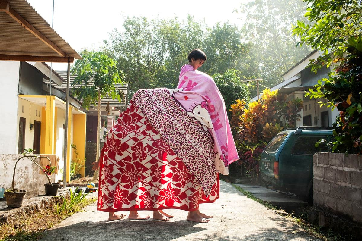 4 people stand in a line covered by three blankets holding aloft a child
