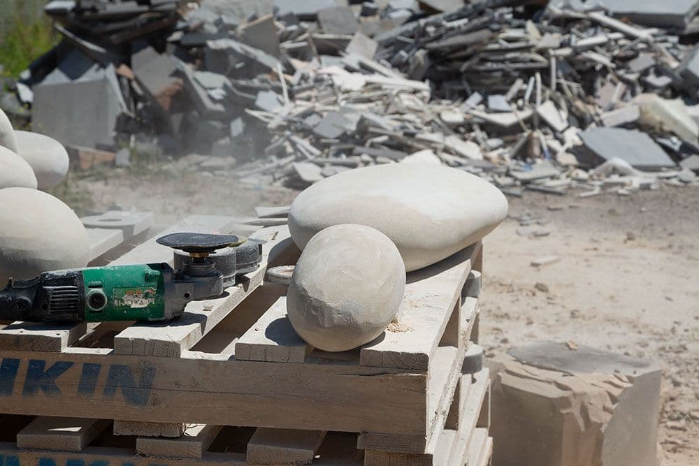 Two carved rocks sit on a wooden pallet next to an angle grinder