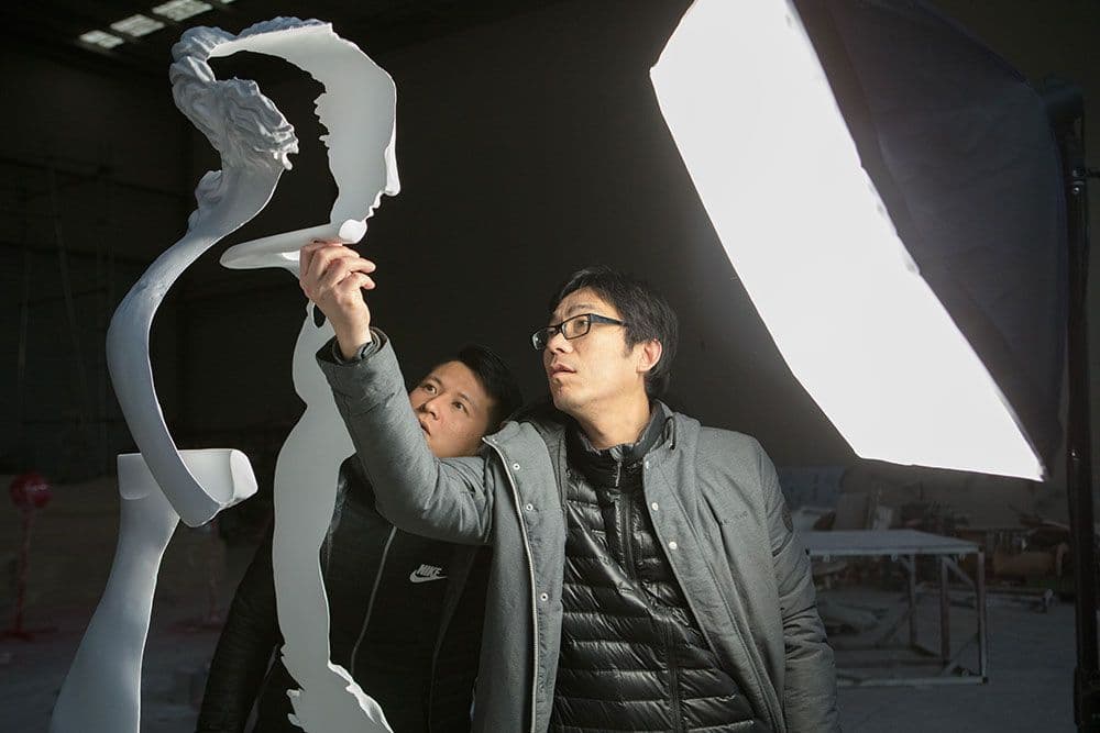 Two people examine a sculpture of a woman