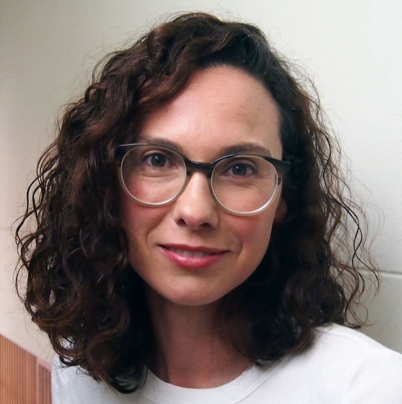 Portrait of young female with dark wavy shoulder length hair wearing glasses and a white t-shirt