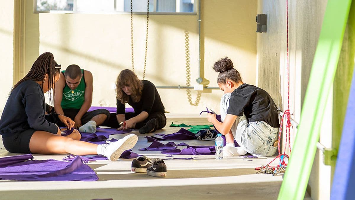 Four people sit on the floor surrounded by purple fabric