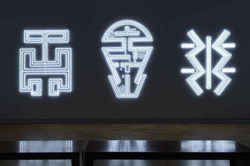 Three large linework neon light designs are hung across a wide wall