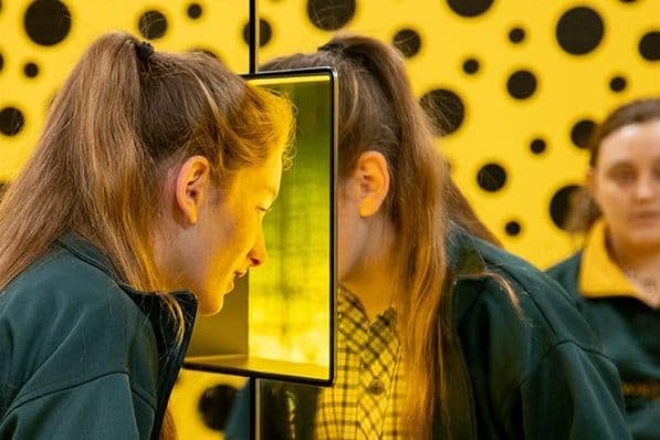 Secondary school aged girl looking through through a mirrored box window as part of an installation.