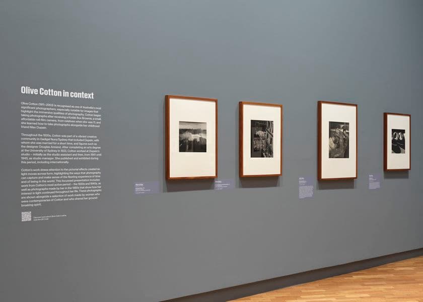A grey wall with an exhibition didactic panel on the left and four works on art on the right