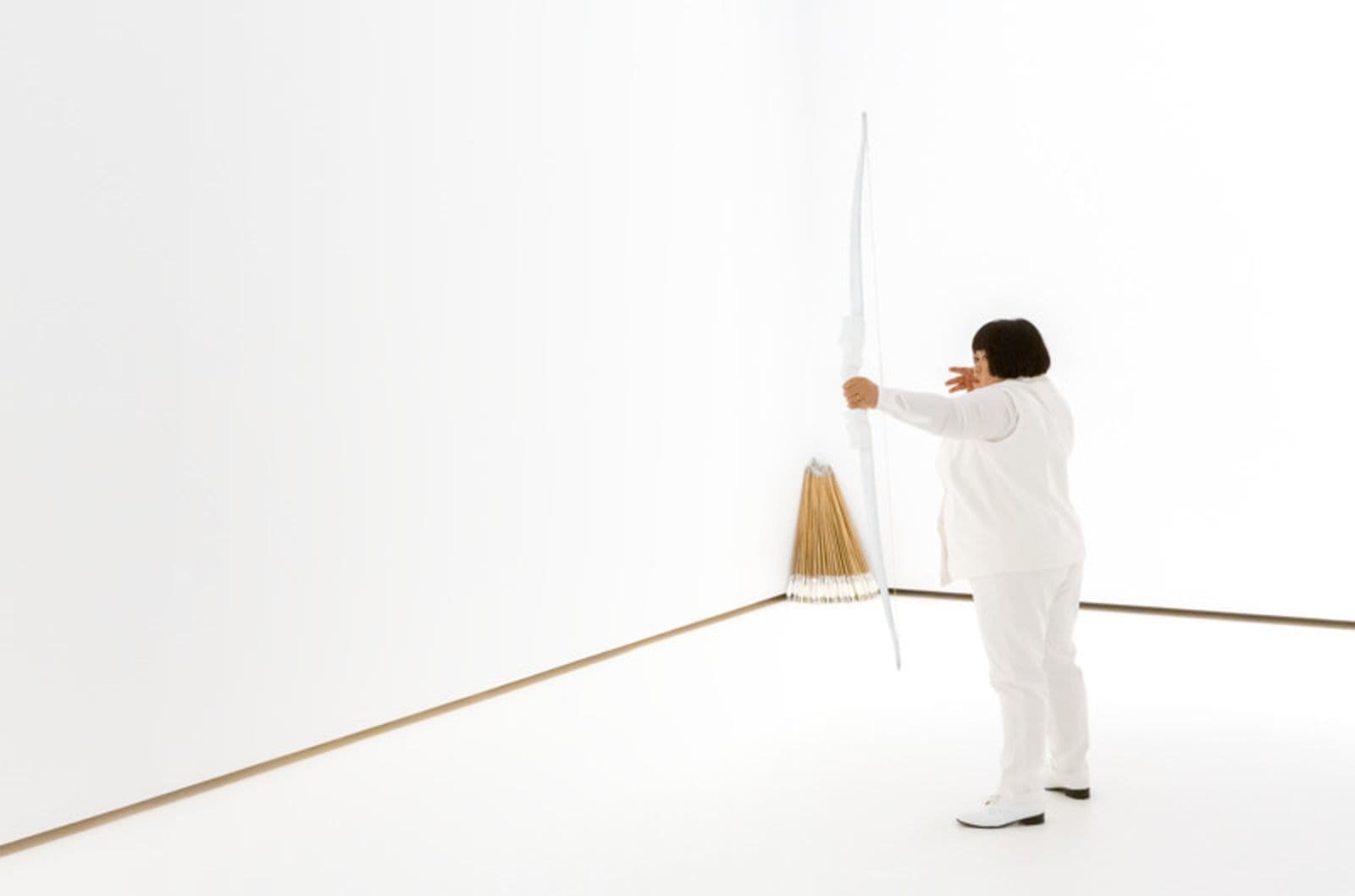 A woman dressed in a white room draws a bow