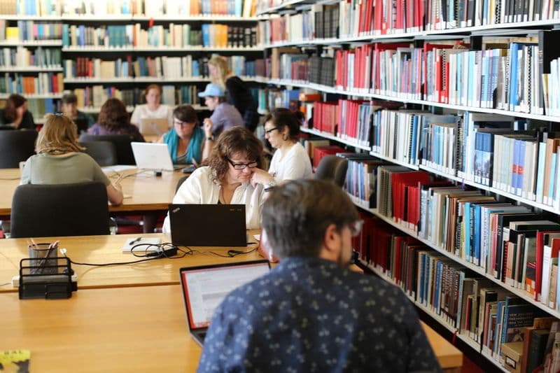 Photograph of people sitting at desks in library in front of book stacks