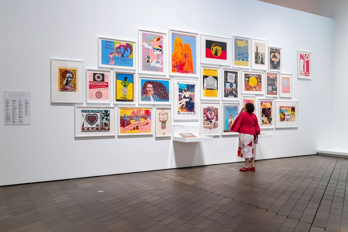 In a large galley space a woman examines a wall of framed and bright posters