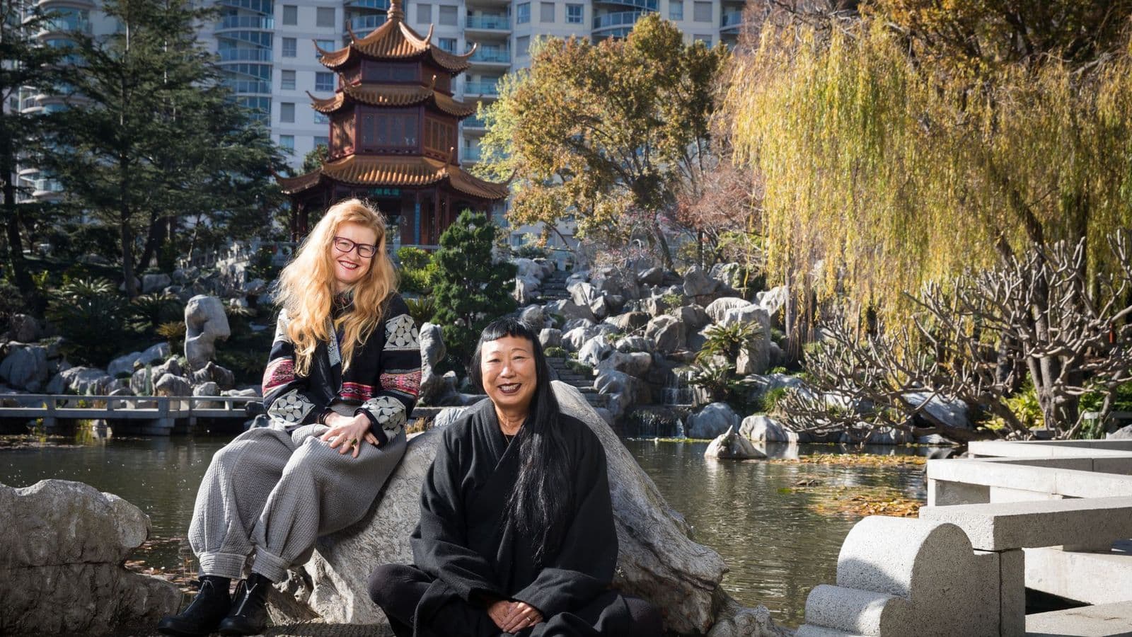 Photo of two women sitting on a rock in a Chinese garden setting
