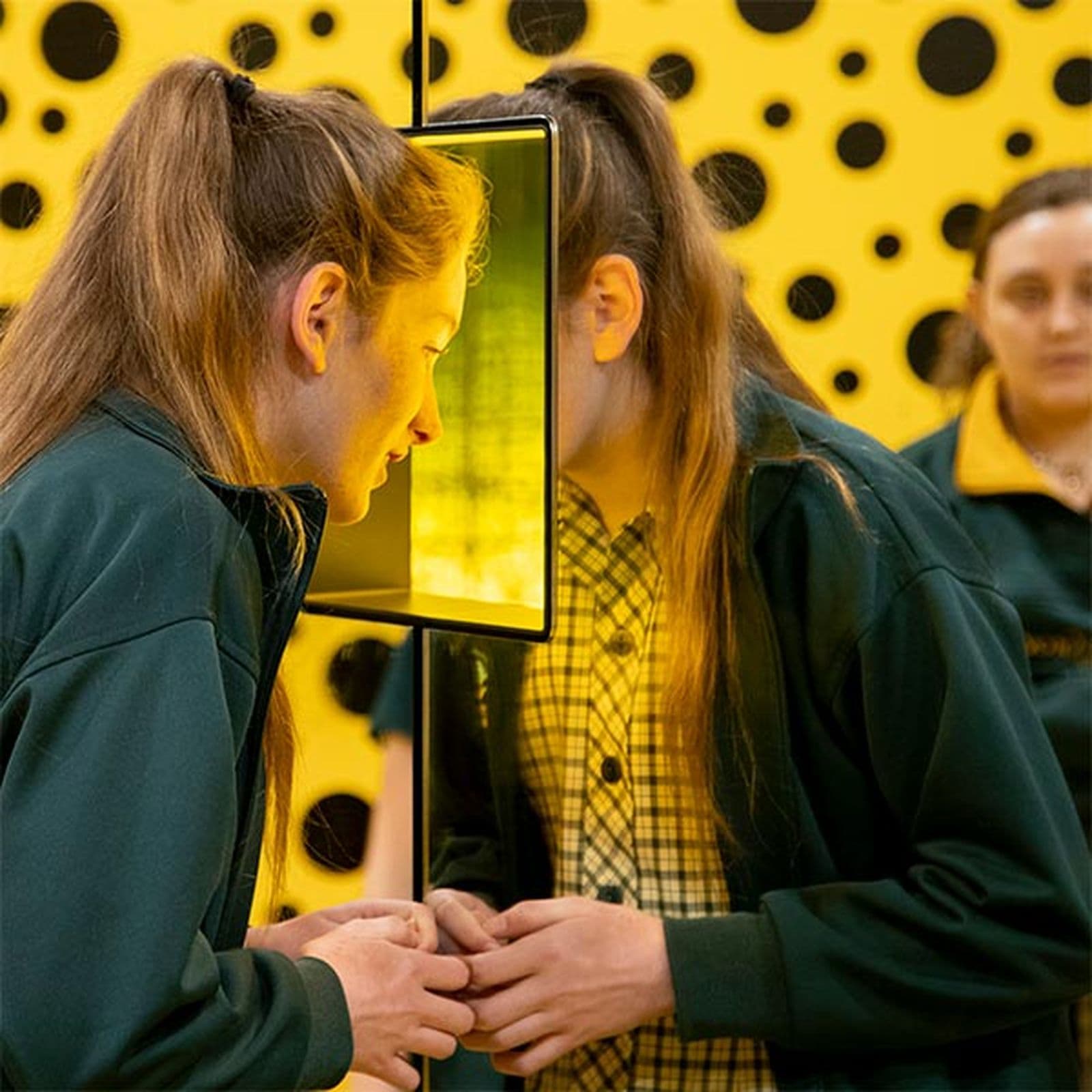 Secondary school aged girl looking through through a mirrored box window as part of an installation.