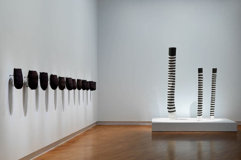 A collection of woven baskets hung along a wall next to three black and white painted poles
