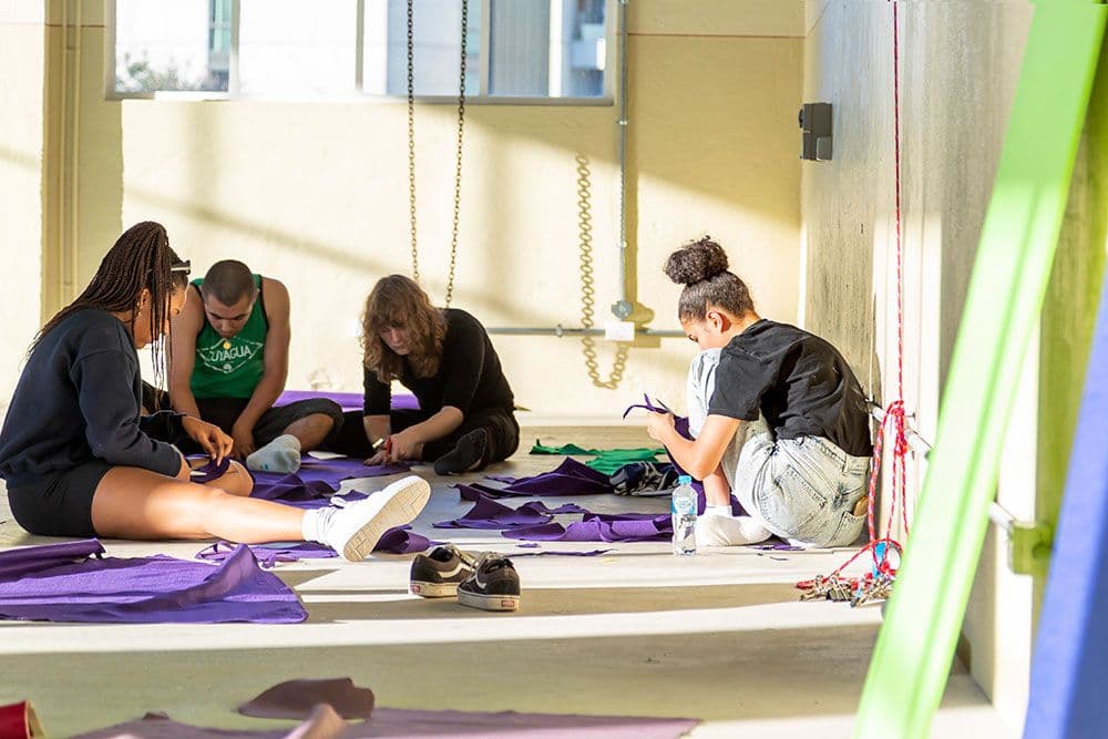 Four people sit on the floor surrounded by purple fabric