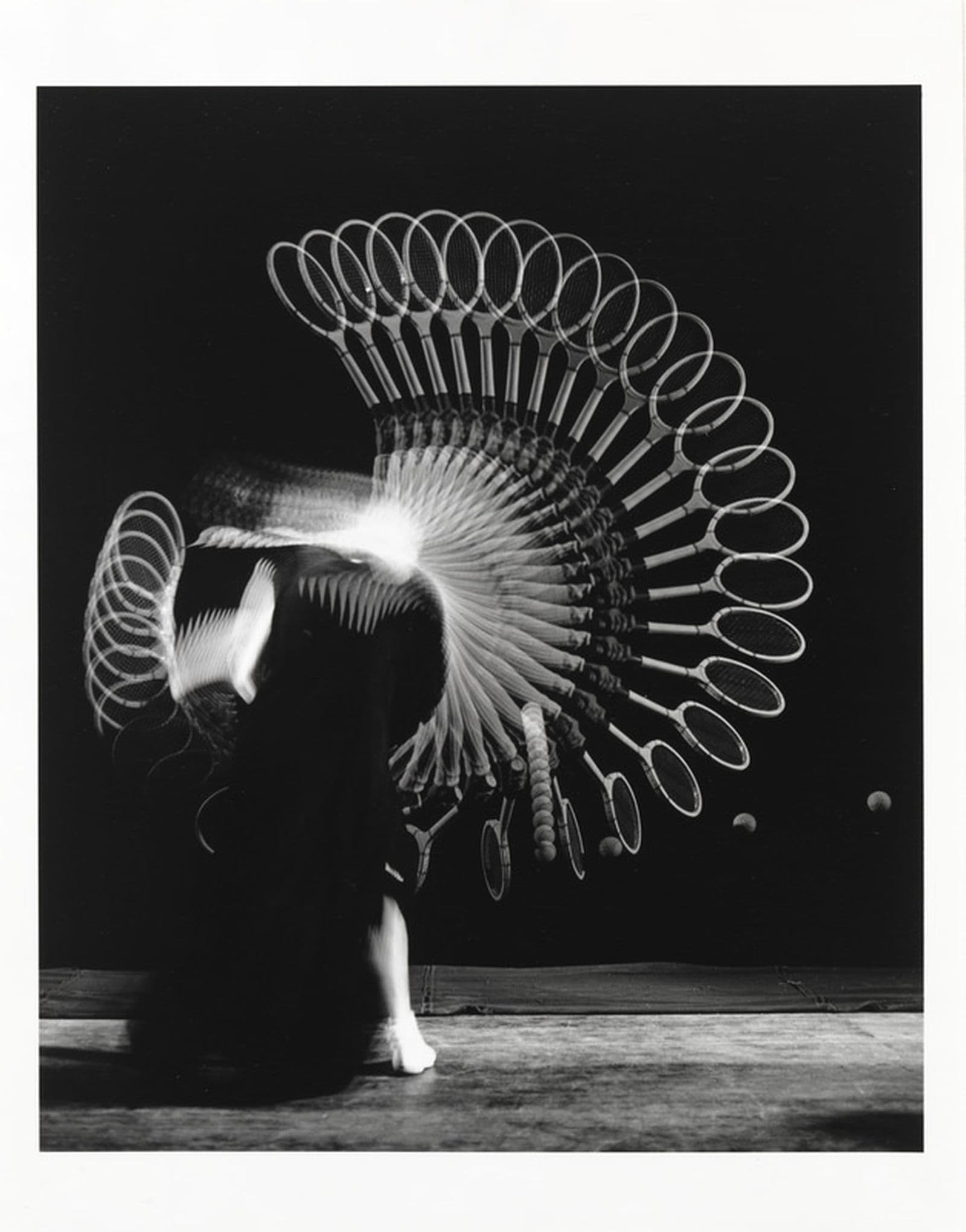 Black and white multi-exposure photograph of a figure with a racket hitting a ball.