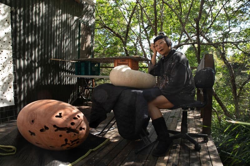 a woman is sitting on a deck at a table with a small sculpture in front of her