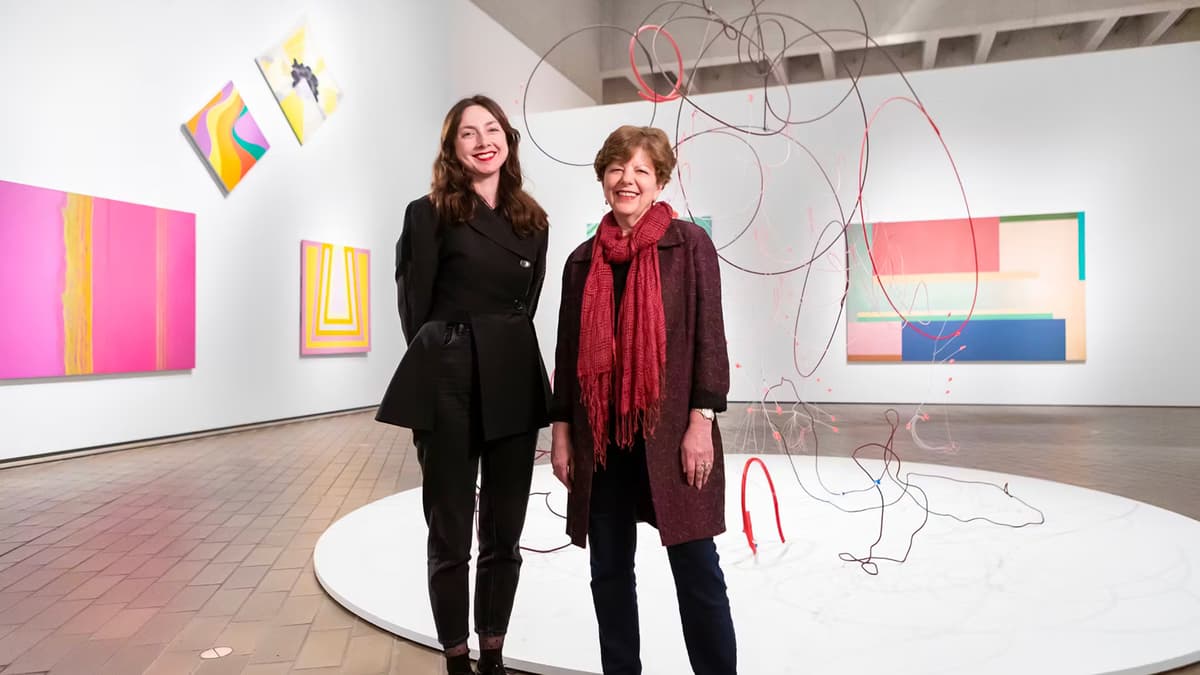 Photo of 2 brunette women inside an exhibition space with colourful artworks