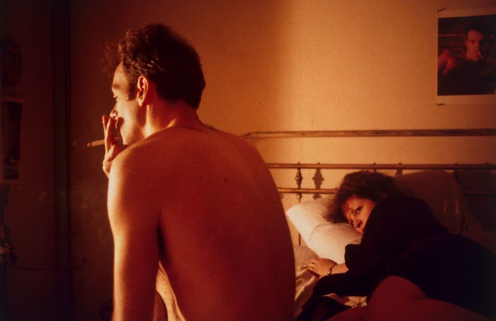 Friend of artist Nan Goldin smoking a cigarette while the artist is laying in bed watching.
