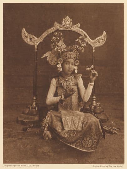 A young Balinese dancer sits while holding a pose, surrounded by a decorative frame