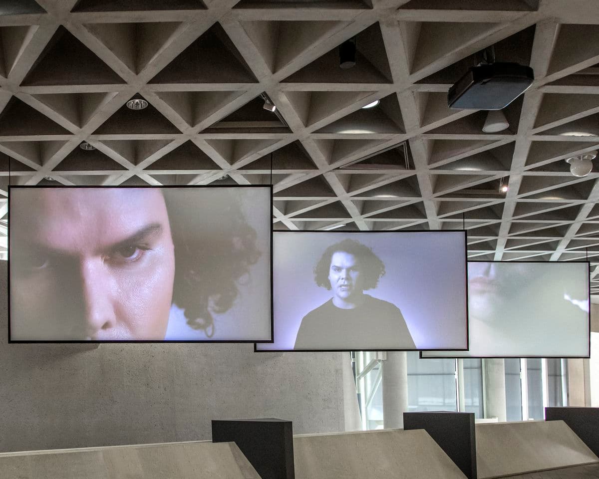 Three large screens hang from the ceiling in a photograph of the Gallery spaces.