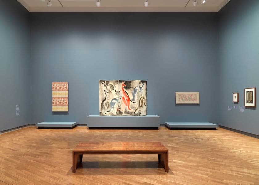 A light grey wall with three works of art hanging on the wall