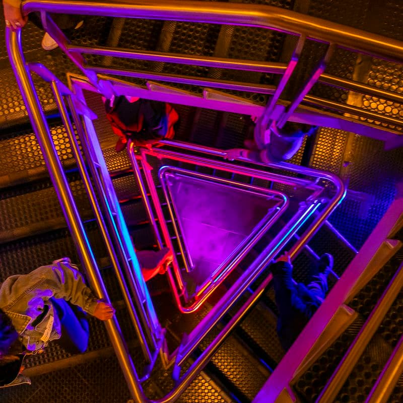 people walking down a triangular staircase