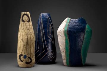 Photo of three ceramic vases positioned alongside each other. They are glazed with different colours and have markings incised on them.