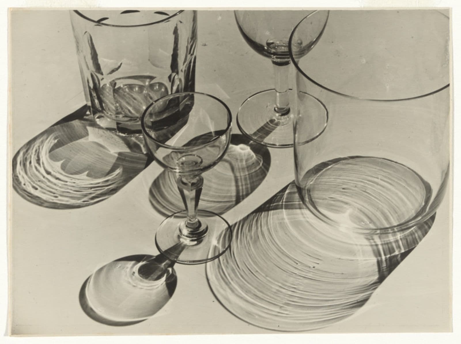 Black and white photograph of drinking glasses of different shapes and sizes casting shadows on the table
